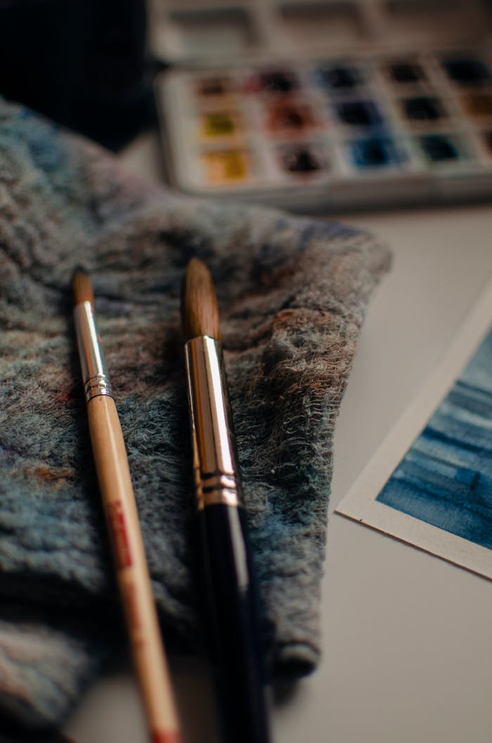 Set of paintbrushes with towel and palette of various colors arranged on white table